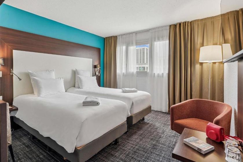 Une élégante chambre twin avec un fauteuil couleur rouille dans l’Hôtel Mercure Paris Porte d’Orléans